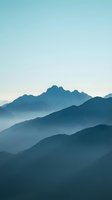 Layered mountain ranges shrouded in atmospheric mist create a serene landscape with misty peaks fading into soft blue tones, suitable for backgrounds and nature designs.