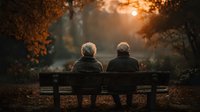 Senior couple sitting together on park bench during golden autumn sunset, enjoying peaceful moment in nature with warm orange foliage and soft sunlight filtering through trees.