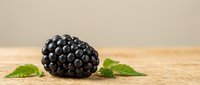Ripe blackberry with fresh green leaves on wooden surface, suitable for food photography, culinary content, and healthy eating promotions.