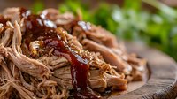 Tender pulled pork with sweet and smoky barbecue sauce served on rustic wooden board, garnished with fresh herbs, close up view of juicy shredded meat.