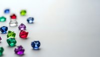 Colorful faceted gemstones scattered on white surface with shallow depth of field creating bokeh effect for jewelry and luxury design projects.