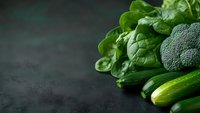Fresh green vegetables including spinach leaves, broccoli and zucchini on dark moody background with copy space. Healthy eating concept for menu design.