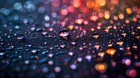 Colorful bokeh lights reflect in water droplets on dark surface creating magical atmosphere with pink, orange and blue glowing circles in defocused background.