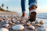 Walking barefoot on beach with seashells at sunset, close up view of feet stepping among white shells on sandy shore with ocean waves and palm trees.