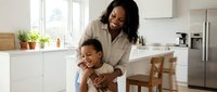 African American mother and young son sharing joyful moment in modern white kitchen. Happy family bonding time at home with natural lighting and contemporary design.