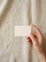 Hand holding blank white business card against neutral beige linen fabric background, suitable for branding, corporate identity, and stationery mockup designs.