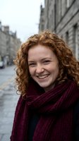 Happy young Caucasian woman with curly red hair wearing burgundy knitted scarf smiling on urban street. Portrait lifestyle photography for marketing campaigns.