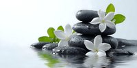 Zen spa composition with stacked black massage stones and white jasmine flowers reflecting in water, creating tranquil wellness atmosphere.