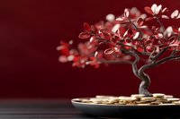 Miniature bonsai tree with red leaves and golden coins on dark burgundy background symbolizing wealth growth and financial prosperity.