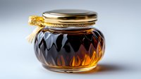 Glass jar with golden honey or amber syrup featuring decorative diamond pattern texture and metal lid with ribbon, illuminated against light background.