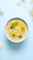 Chia seed pudding with mango puree swirl and fresh mint leaves in ceramic bowl on light blue background for healthy breakfast recipes.