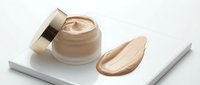 Luxury beige foundation cream jar with golden cap and makeup smear on white marble tray for cosmetic branding and beauty product advertising.