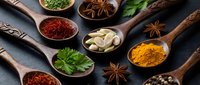 Aromatic spices and herbs in wooden spoons on dark slate background. Culinary ingredients including turmeric, saffron, star anise for cooking and seasoning.