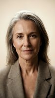 Mature woman with long gray hair wearing neutral blazer against beige background. Professional headshot suitable for corporate, business, and editorial use.