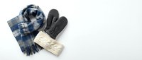 Winter accessories flat lay with blue plaid scarf, gray mittens and cream knit hat on white background for seasonal fashion and cold weather styling.