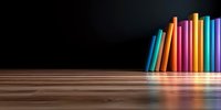 Row of colorful books standing on wooden surface against dark background with rainbow reflection, minimalist education and literature concept.