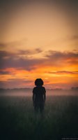 Silhouette of young African American woman standing in misty field during golden hour sunrise with dramatic orange and purple sky clouds.