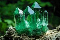 Vibrant emerald green crystal cluster formation on rough stone base with natural forest background, showcasing translucent mineral points and prismatic structure.
