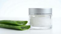 Fresh aloe vera leaves with natural gel extract in glass jar for skincare and cosmetic applications on clean white background.