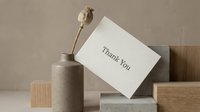 Minimalist thank you card leaning against geometric blocks with a dried poppy stem in a ceramic vase, neutral beige tones, elegant and modern style.