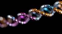 Sparkling crystal beads in vibrant purple, blue and gold colors form elegant spiral pattern against dark background, creating luxurious jewelry design element.