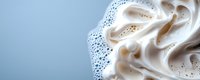 Soft peaks of whipped cream or meringue with delicate foam texture against light blue background, macro food photography with copy space for dessert menu.