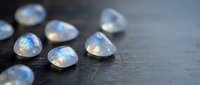 Moonstone gemstones with blue flash adularescence scattered on dark wooden surface for jewelry making and crystal healing practices.