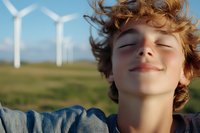 Young woman with curly hair enjoying fresh air at wind farm, eyes closed in peaceful moment, renewable energy and environmental sustainability concept.
