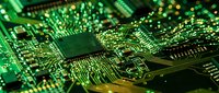 Green circuit board with microchip and electronic components showing intricate pathways and connections for technology and computing applications.
