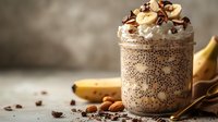 Chia seed pudding topped with whipped cream, chocolate shavings, and almonds, served with fresh banana for healthy breakfast or dessert preparation.