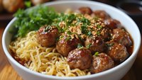 Savory meatballs with fresh herbs served over golden pasta noodles in white bowl, comfort food meal ready for dinner table presentation.