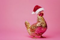 Festive rooster wearing red Santa hat with gold and pink glitter coating stands against pink background, perfect for holiday greeting cards and seasonal marketing materials.