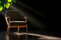 Modern gray armchair with wooden frame in dramatic lighting against dark wall, sunbeams through leaves create natural spotlight effect on minimalist furniture piece.