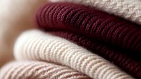 Cozy stack of folded knitted sweaters in burgundy and cream colors showing soft wool texture and warm winter clothing details in natural lighting.