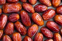Fresh ripe dates arranged in rows showing natural variations in color from bright orange to deep red, glossy surface texture creates appetizing pattern.