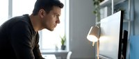 Young professional man concentrating while working on computer in modern office environment with natural lighting and contemporary workspace setup.