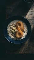 Overhead view of caramelized pear halves served in dark bowl with creamy oatmeal porridge and fresh rosemary garnish on rustic wooden table, ideal for food styling and culinary content.