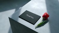 Elegant black thank you card with red tulip on concrete surface in soft natural light, minimalist style for greeting and appreciation designs.