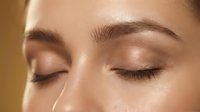 Close-up of young woman's face with natural makeup and glowing skin. Eyes closed showing long eyelashes and defined eyebrows. Skincare and beauty concept.