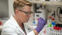 Laboratory scientist in white coat and protective gloves conducting precise pipette work with test tubes and samples in modern research facility setting.