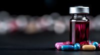 Medical vial with red liquid and colorful pills scattered on dark background with bokeh effect. Healthcare and pharmaceutical concept.