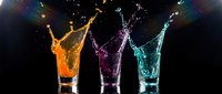Colorful liquid splashing from three glasses creating dynamic motion against dark background for beverage advertising and party concepts.
