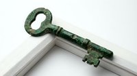 Antique green patina metal key with ornate handle resting on white wooden surface, isolated on neutral background, suitable for vintage design, historical projects, and decorative applications.