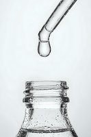 Clear water drop falling from glass dropper into bottle neck, captured in high contrast black and white macro photography against white background.