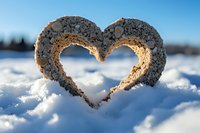 Heart shape drawn in fresh snow with sunlight shining through creating warm glow against bright blue winter sky background, romantic winter scene outdoors.