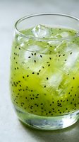 Refreshing kiwi cocktail or mocktail with ice cubes and seeds in a glass, vibrant green color, close-up shot on light background.