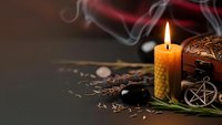 Mystical altar setup with burning beeswax candle, pentagram pendant, herbs and ritual tools creating atmospheric witchcraft scene for spiritual practices.