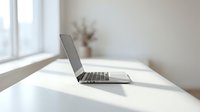 Modern laptop computer open on white desk in bright minimalist office workspace with natural window light and decorative plant creating productive work environment.