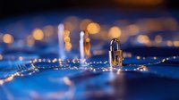 Small padlock on digital circuit board with glowing connections and bokeh lights in background, representing cybersecurity and data protection concept.