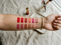 Lipstick color swatches on woman arm showing various shades from red to nude for makeup testing and beauty product selection.